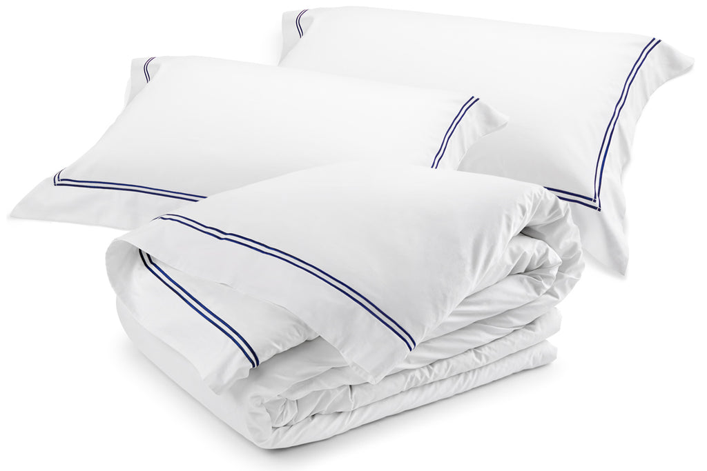 White cotton sateen duvet cover set with navy satin-stitch embroidery, including two pillowcases, neatly styled in a folded stack.