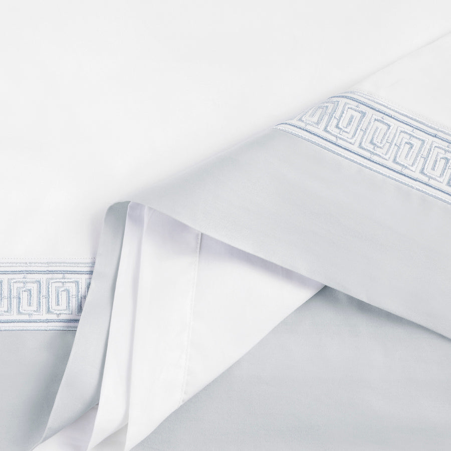 Close-up view of Flaxfield Linen's Rhodes Flat Sheet Set showcasing the detailed Meander pattern embroidery in Grecian Blue on luxurious 400-thread count cotton sateen fabric