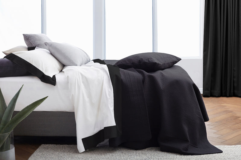 Resort sheet set with black European border styled on a bed with white flat sheet and black bedding accents.