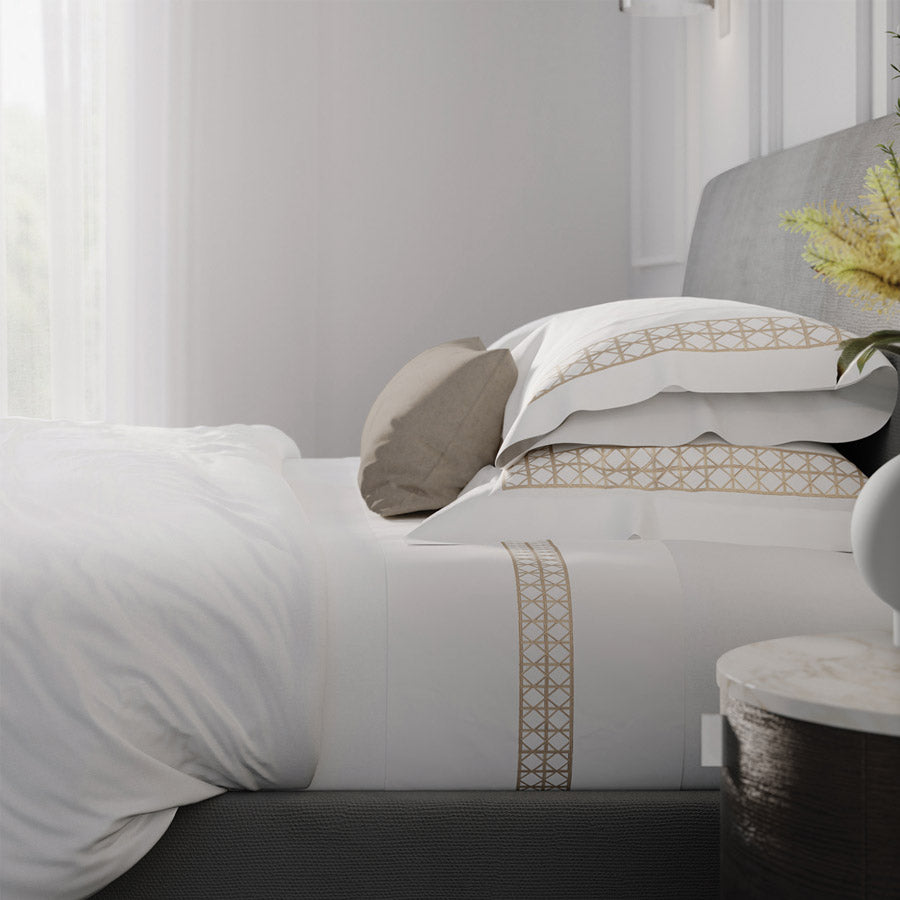 Bedroom setting with white rattan-embroidered pillowcases and matching sheet set on a grey upholstered bed