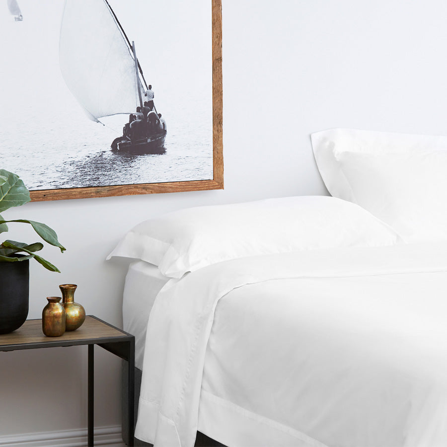 White Resort sheet set styled on a bed with European turnback detail, cuffed pillowcases and a coastal-inspired framed artwork above the bedside table.